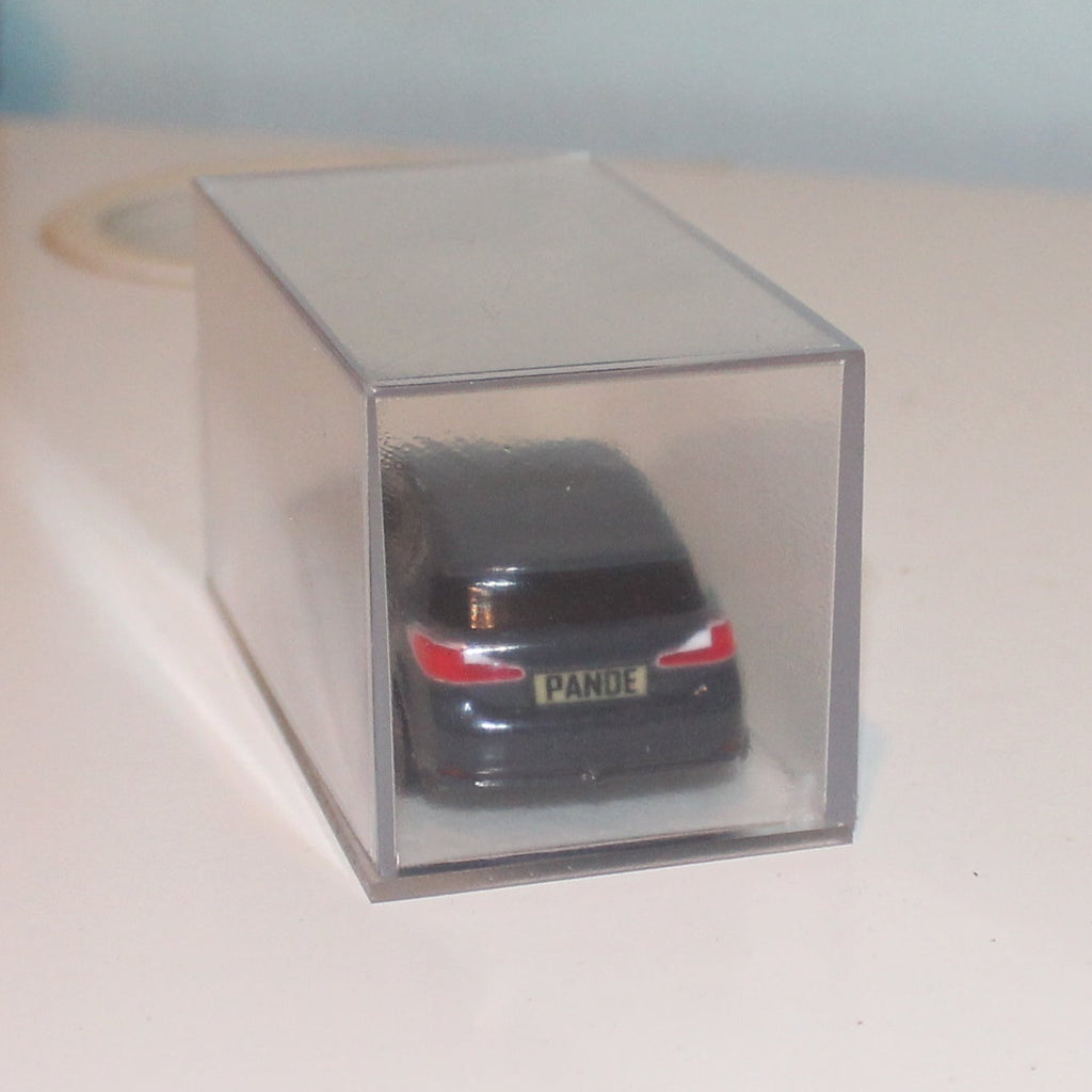 Small model car in a clear box on a desk with a plain background