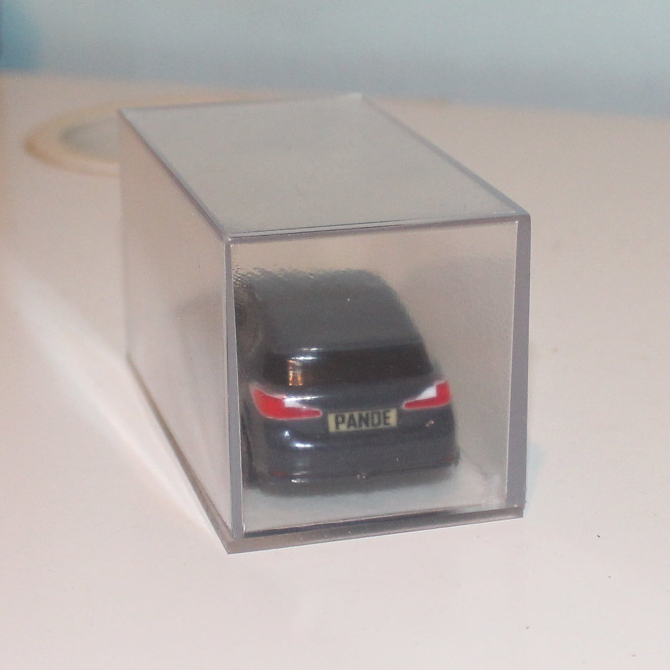 Small model car in a clear box on a desk with a plain background